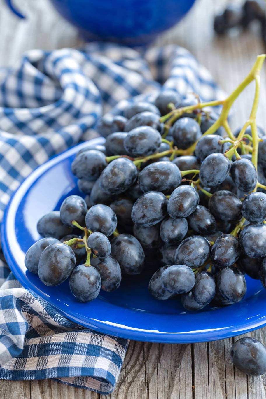 Cynthia Grape A bundle of bluish purple cynthia grapes sitting on a blue plate